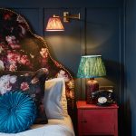 Hotel bed decorated with blue pillows and a floral backboard. Vintage lamp and telephone on the side table.