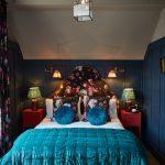 Hotel bed decorated with blue pillows and a floral backboard.