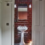 Door opening to bathroom sink. Bathroom has a bright red bricked wall.