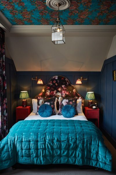 Hotel bed with aqua blue backboard. Side table is decorated with vintage radio.